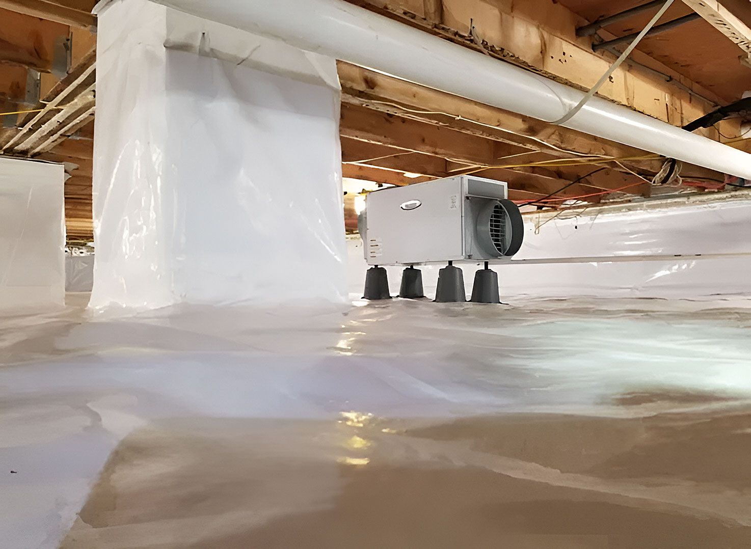 Low crawlspace beneath a house with plastic vapor barrier and exposed wooden beams.