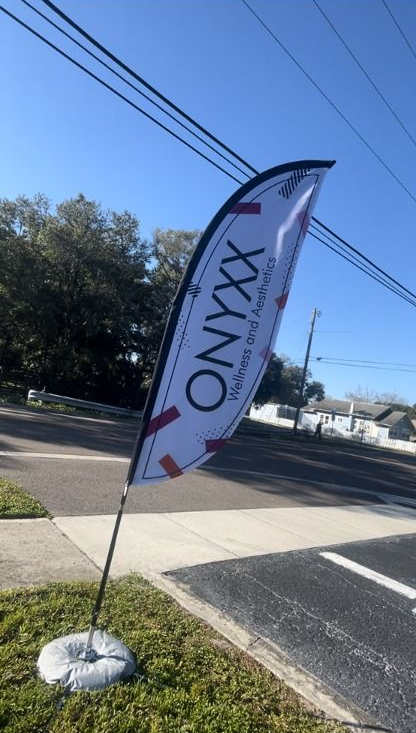 A white Onyxx banner with logo is staked to a sidewalk, set against a street and blue sky.