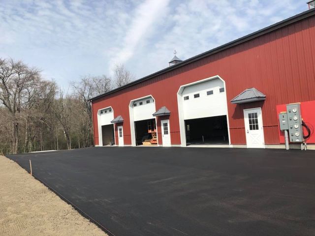 A red barn with white doors and a black driveway in front of it.