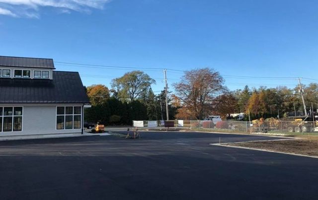 A white building with a black roof is sitting next to a parking lot.
