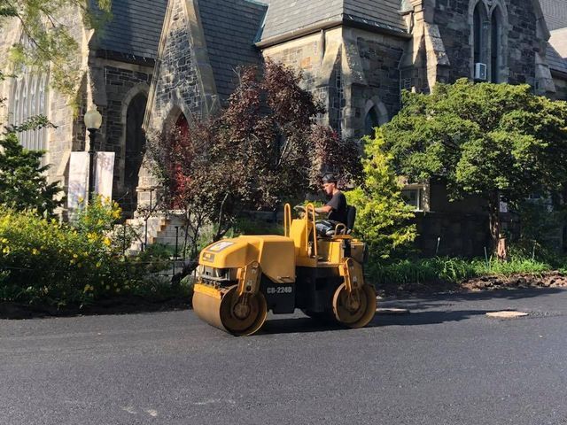 A man is driving a yellow roller on a road in front of a church.