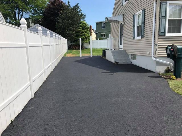 A driveway leading to a house with a white fence