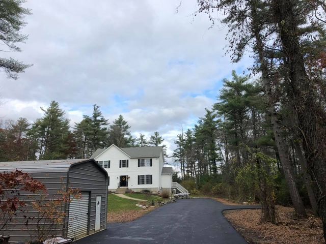 A large white house is surrounded by trees and a driveway.