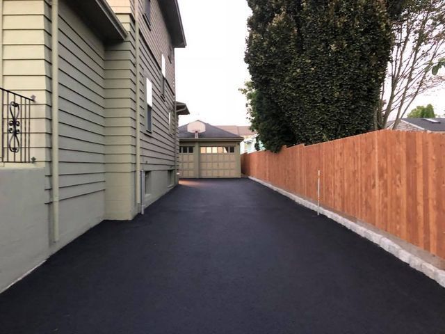 A driveway leading to a house with a wooden fence
