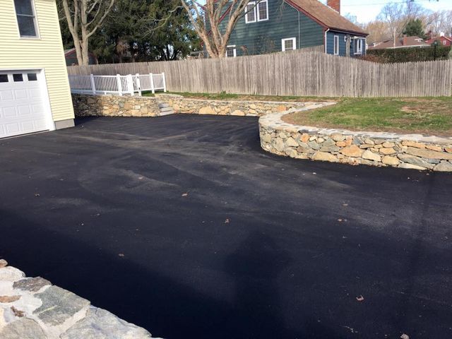 A driveway with a stone wall and a fence in front of a house.