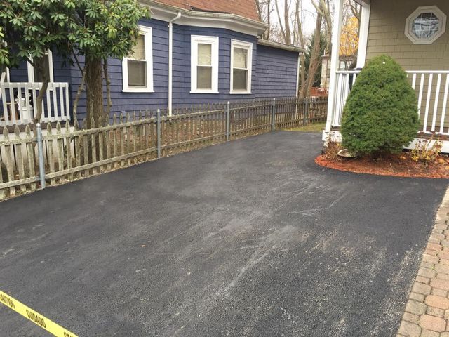 A driveway in front of a blue house with a white fence