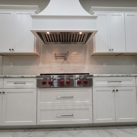 A kitchen with white cabinets , a stove top oven , and a hood.