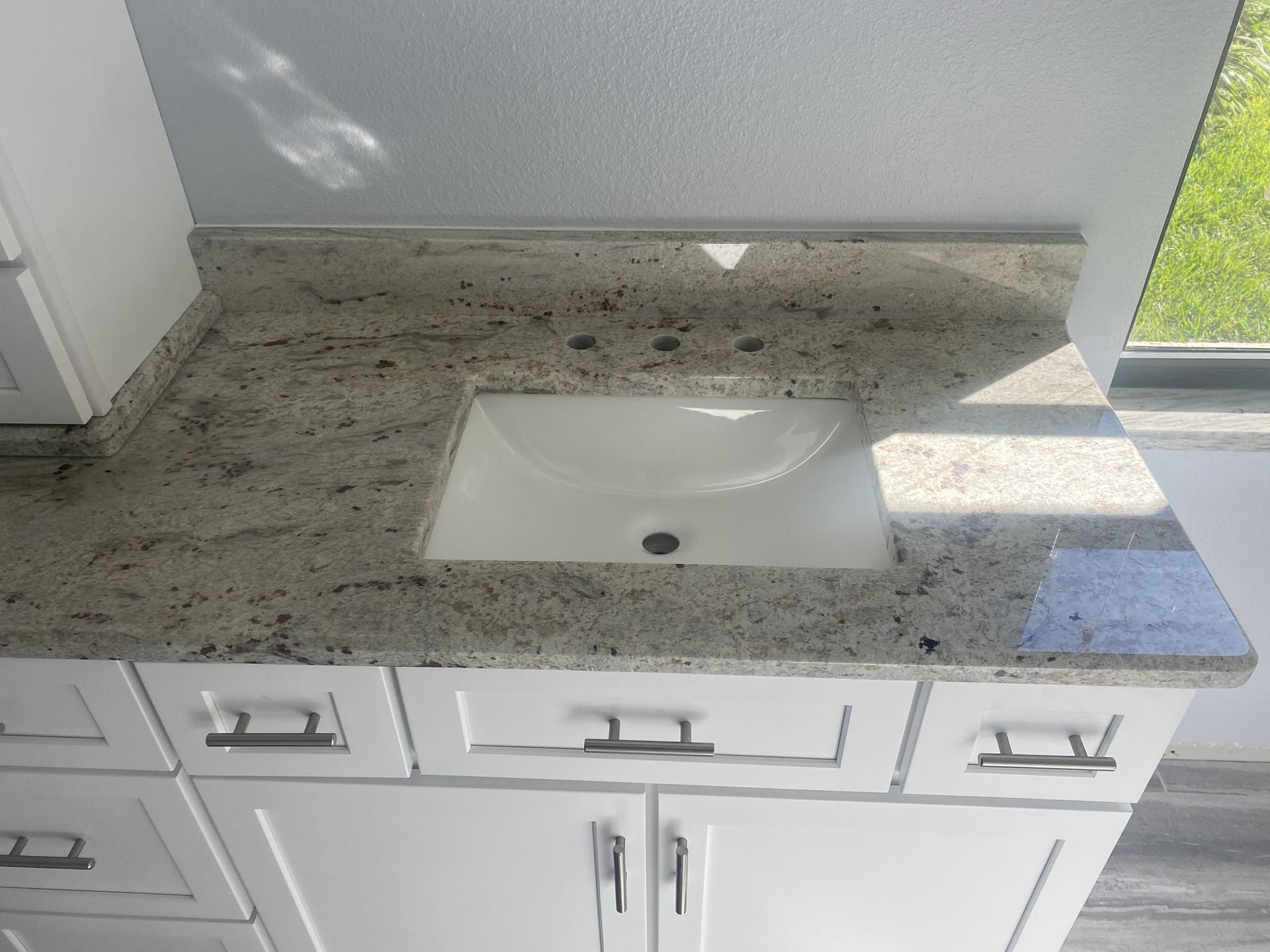 A bathroom sink with a granite counter top and white cabinets