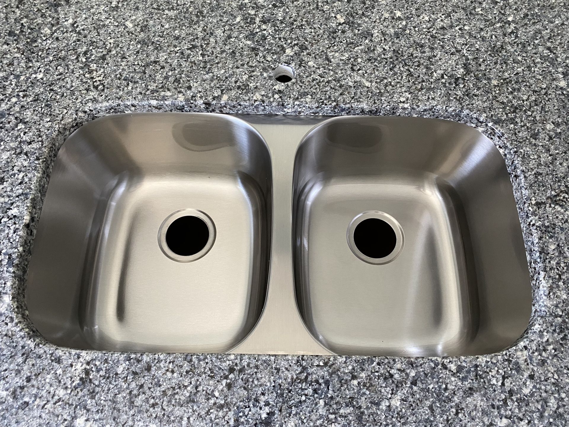 A stainless steel kitchen sink is on a granite counter top.