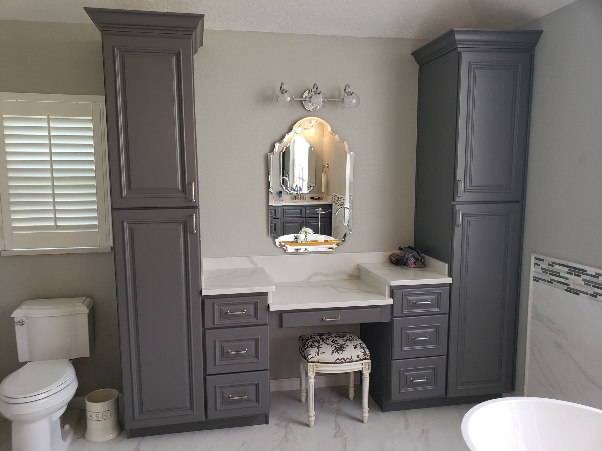A bathroom with gray cabinets, a toilet, a sink and a mirror