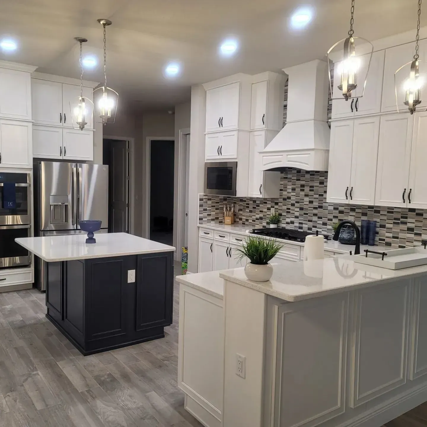 Modern kitchen with white cabinets, dark blue island, stainless steel appliances, and pendant lights.