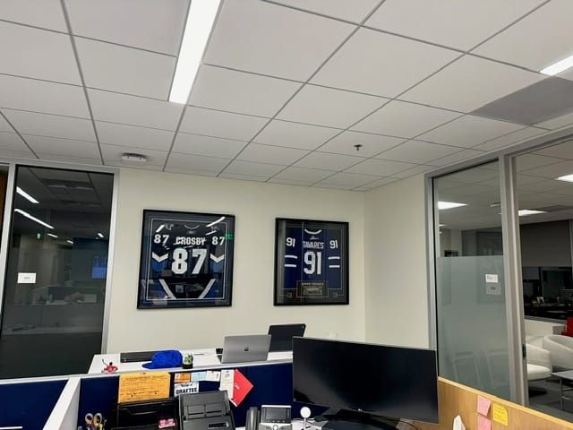 Office with framed football jerseys, cubicles, computers, and overhead lighting.