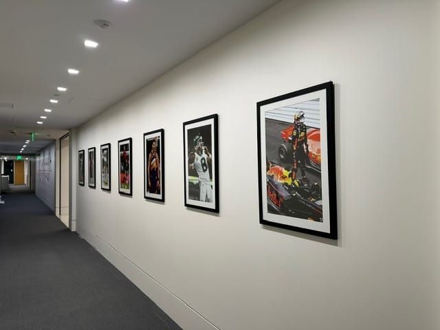 Long hallway with framed sports art on white walls, illuminated by ceiling lights.