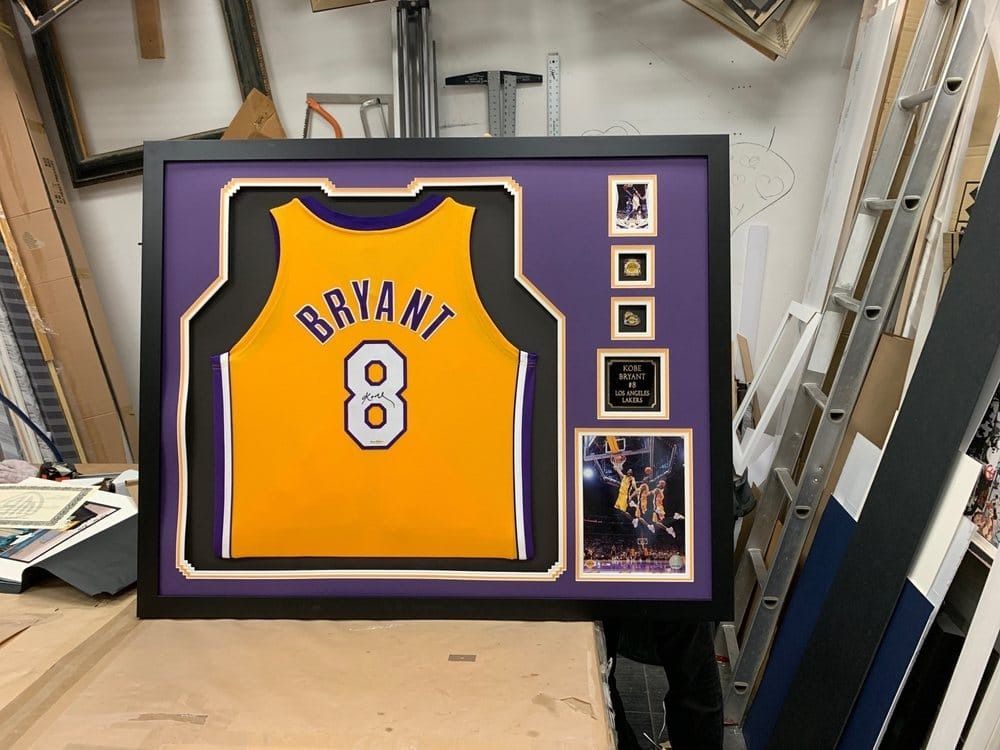 Framed Kobe Bryant Lakers jersey and memorabilia in a shadow box, with purple and gold accents.