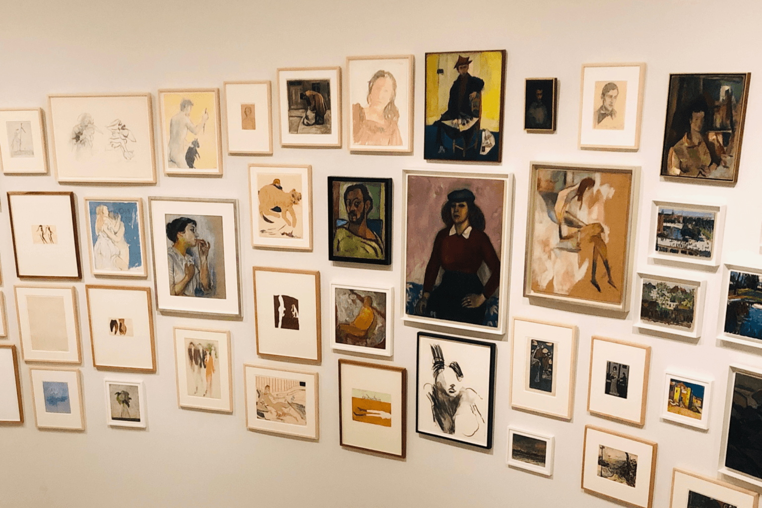 Wall of framed artwork, various sizes, styles, and subjects, in a gallery setting.