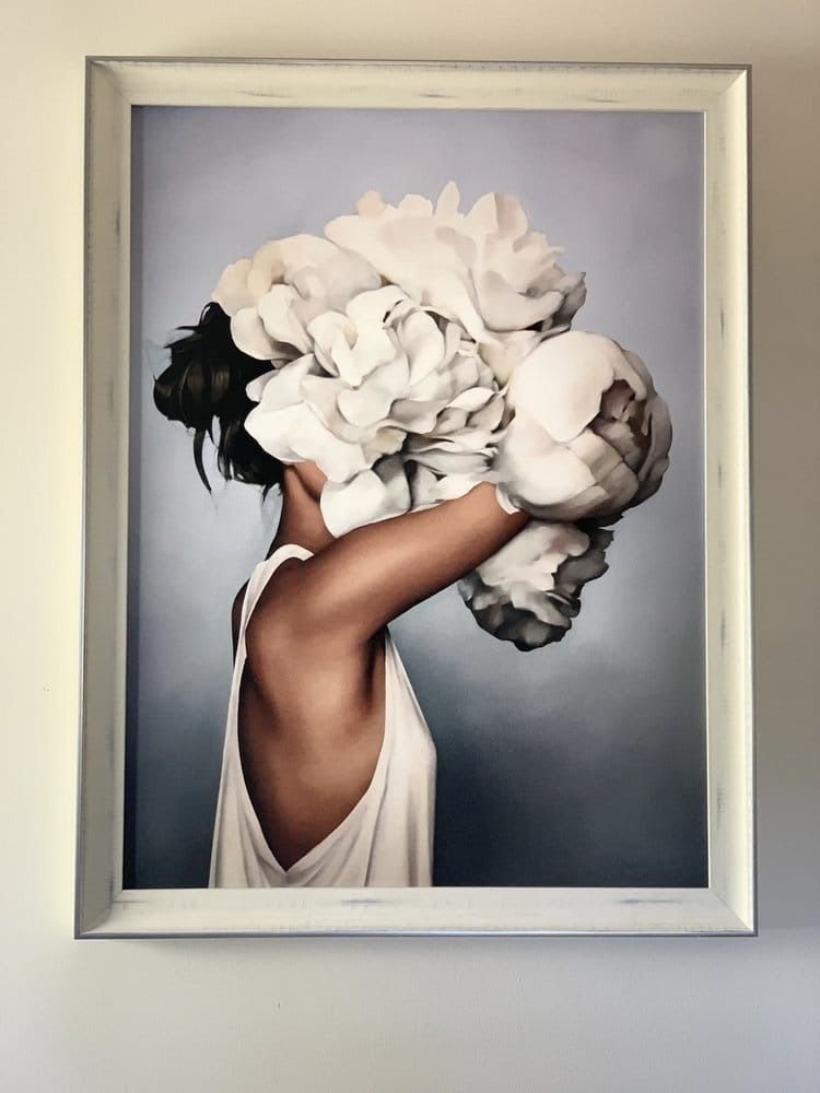 Woman with dark hair obscured by large white flowers, wearing a white dress against a gray backdrop.