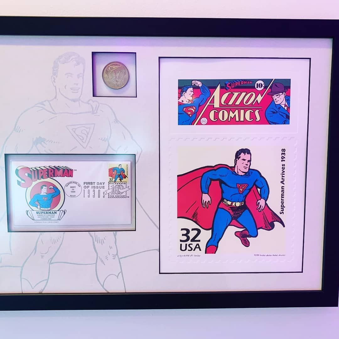 Framed Superman memorabilia: stamps, coin, and a sketch. Black frame on a white background.