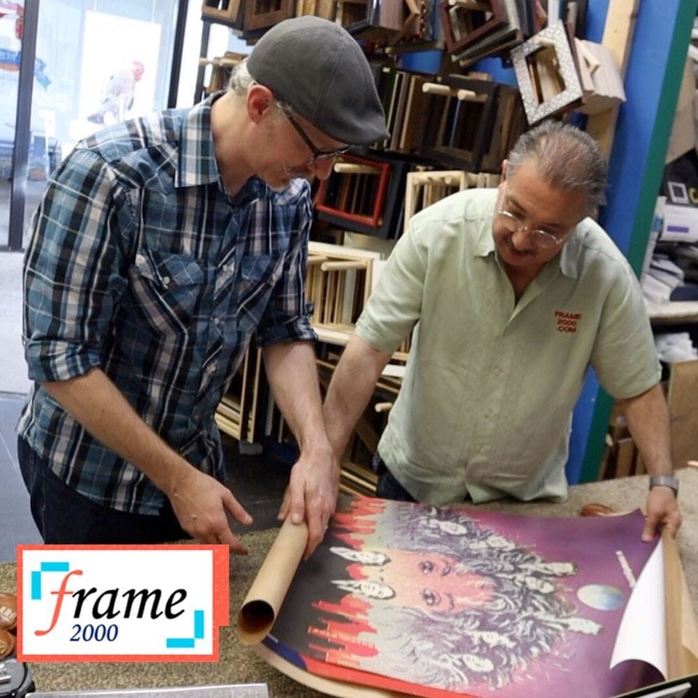 Man examines print from printer, framed artwork in background.