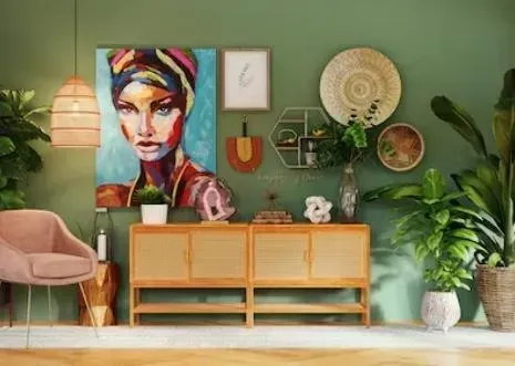 Green wall with art, decor, and plants. A cabinet sits below a woman's portrait. A pink chair and lamp on the left.