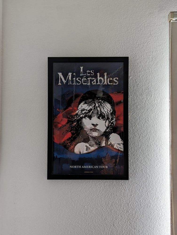 Les Misérables poster in black frame, hangs on a textured white wall.