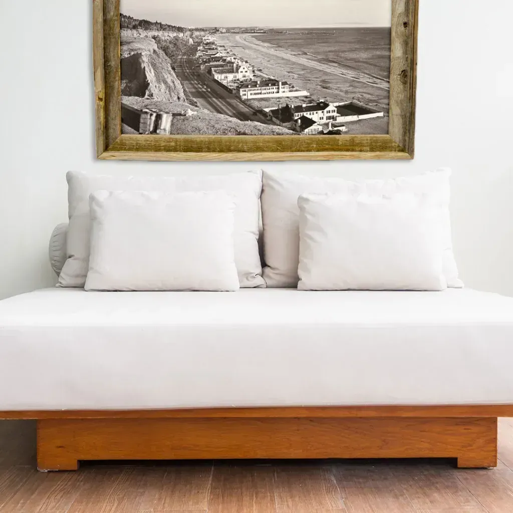 White daybed with pillows and framed coastal landscape on white wall.