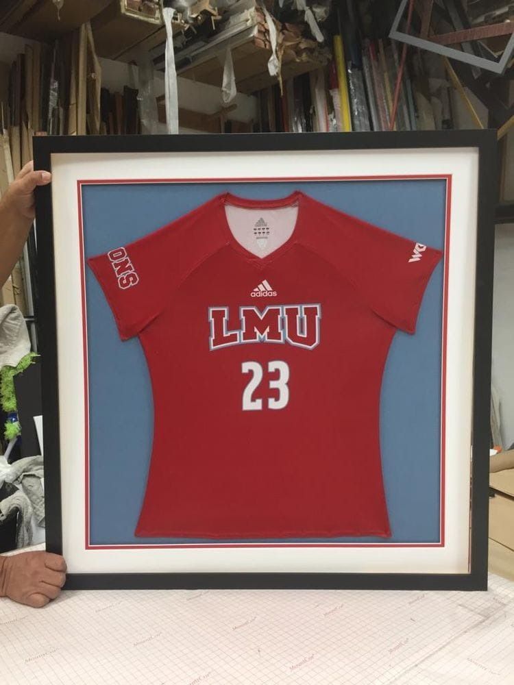 Framed red LMU volleyball jersey with number 23 on blue background, held by a person.