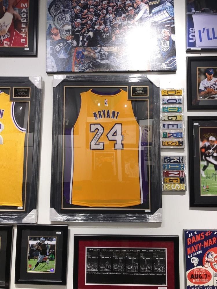 Kobe Bryant Lakers jersey, framed, on a wall with other framed memorabilia, including tickets, photographs and additional jerseys.