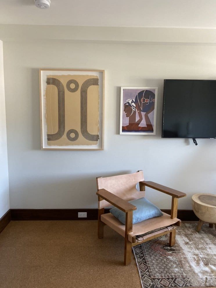 Living room with artwork, chair, and rug. Beige walls, brown trim. Wood chair, pink cushion, blue pillow.