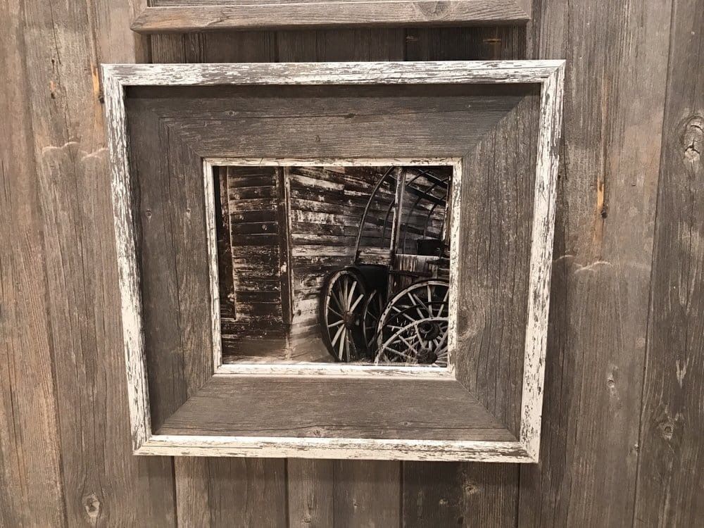 Framed black and white art of wagon wheels inside a weathered wooden structure. The frame is gray and white.