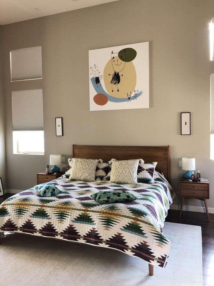 Bedroom with bed, art, and two nightstands. Soft colors, geometric quilt, and abstract artwork.