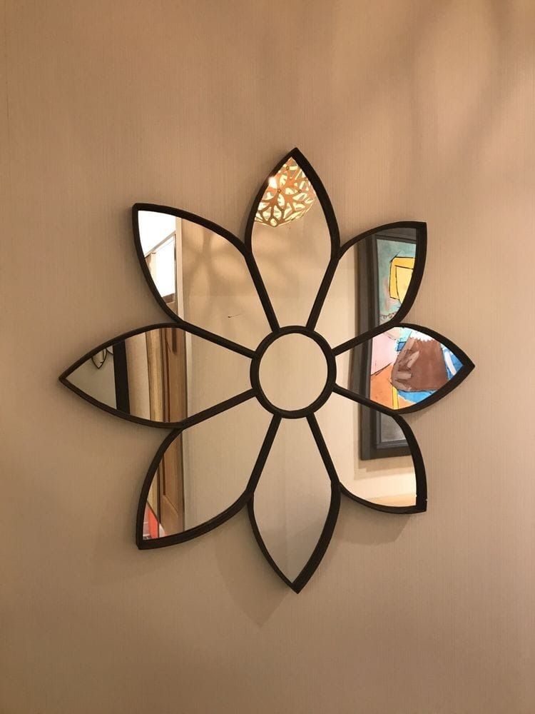 Flower-shaped mirror with dark frame on a light-colored wall, reflecting room details.