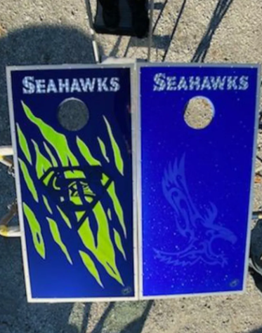 Two blue Seahawks cornhole boards with neon green bird designs and circular holes, outdoors on concrete.