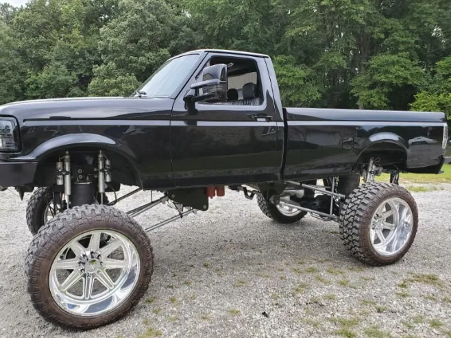 Lifted black pickup truck with oversized chrome wheels parked on gravel in front of trees
