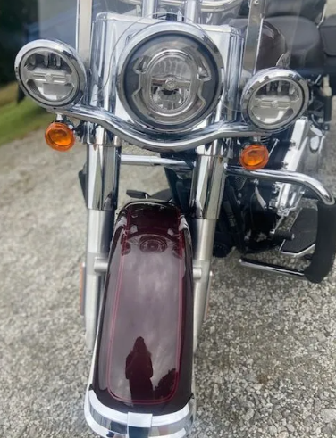 Front view of a chrome motorcycle with round headlights and a maroon fender on pavement