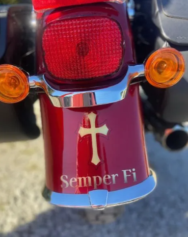 Close-up of a red motorcycle tail light with a white cross and “Semper Fi” text on the fender