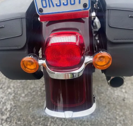 Rear view of a maroon motorcycle with red taillight, amber turn signals, and saddlebags.