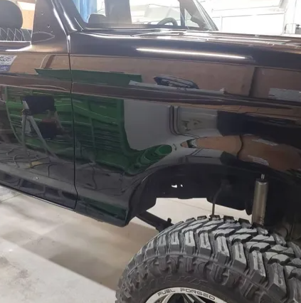 Black off-road truck side with large tires in a garage, showing a lifted suspension.