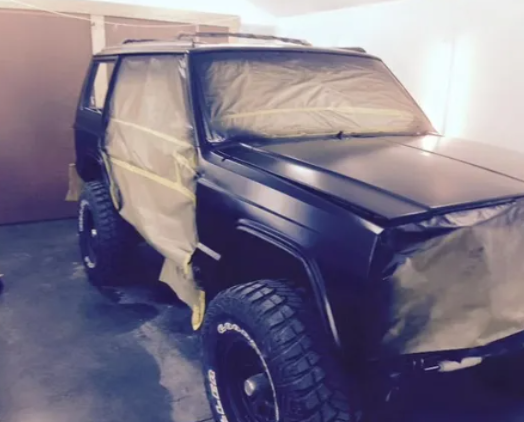 Black SUV masked with tape and plastic in a garage, likely being painted or repaired