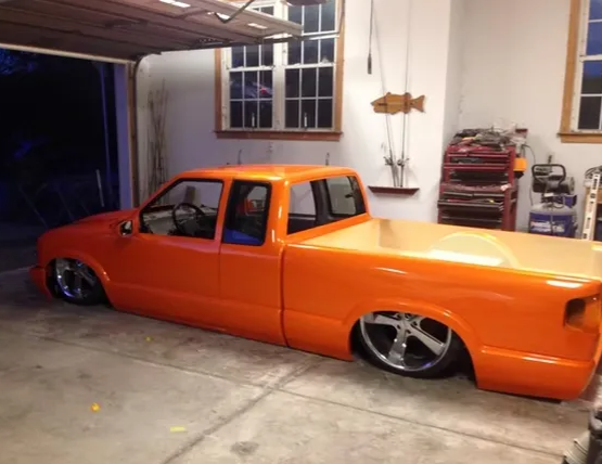 Orange lowered pickup truck parked in a garage at night, with chrome wheels and custom bodywork