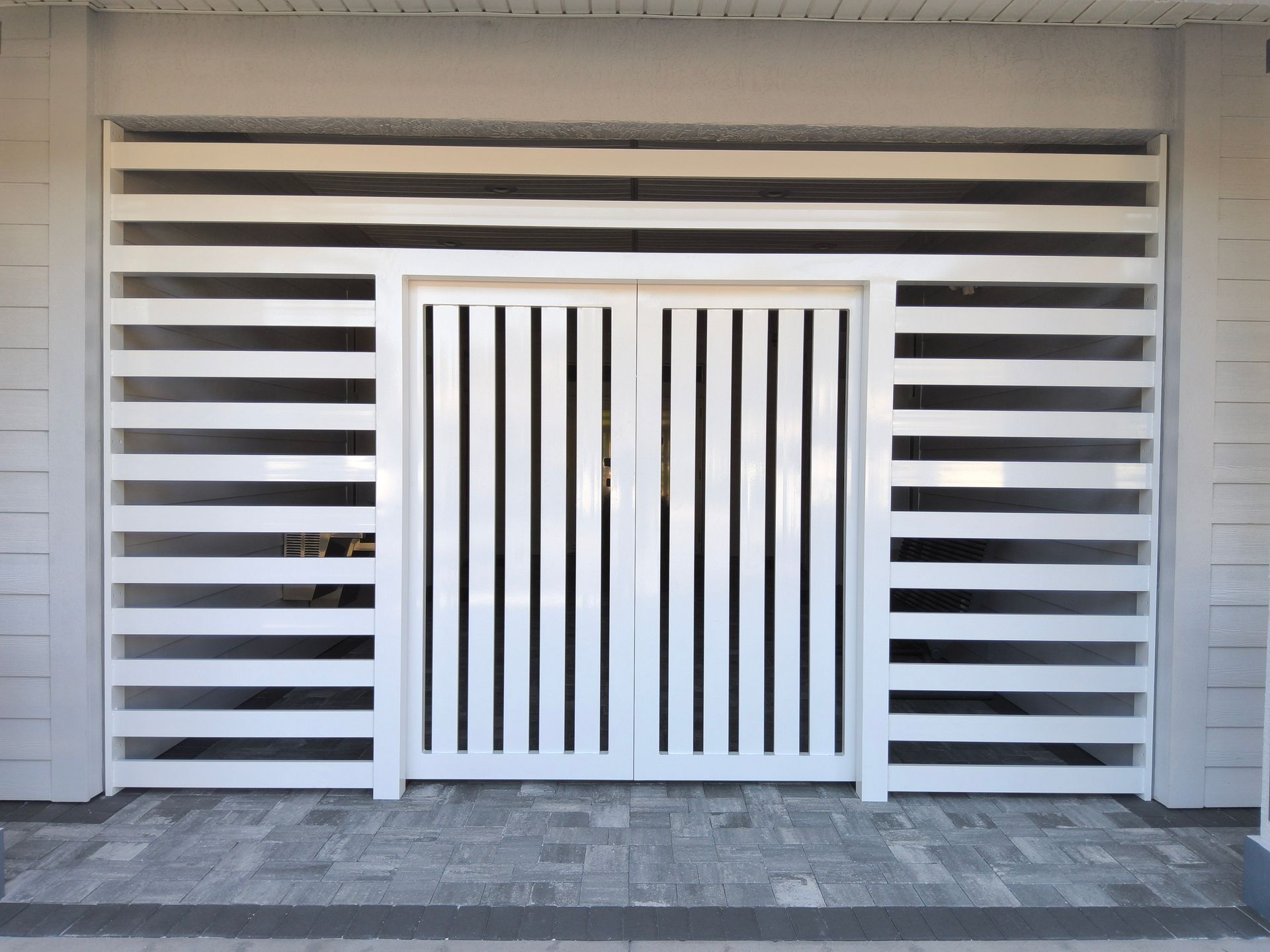 White gate with vertical slats, flanked by horizontal slat walls, set in a gray tiled entryway.