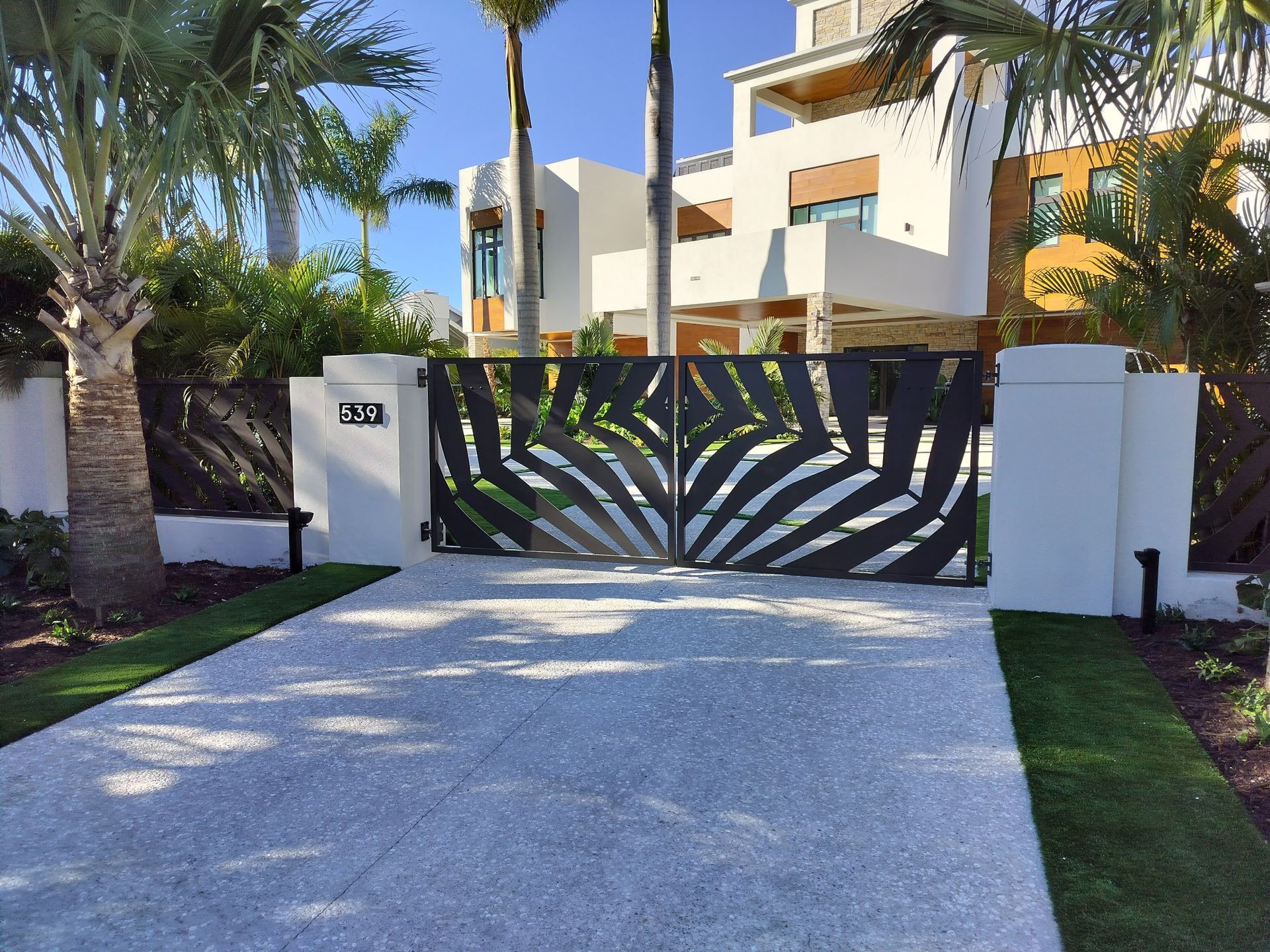 Modern home with white facade, ornate black gates, and gravel driveway.