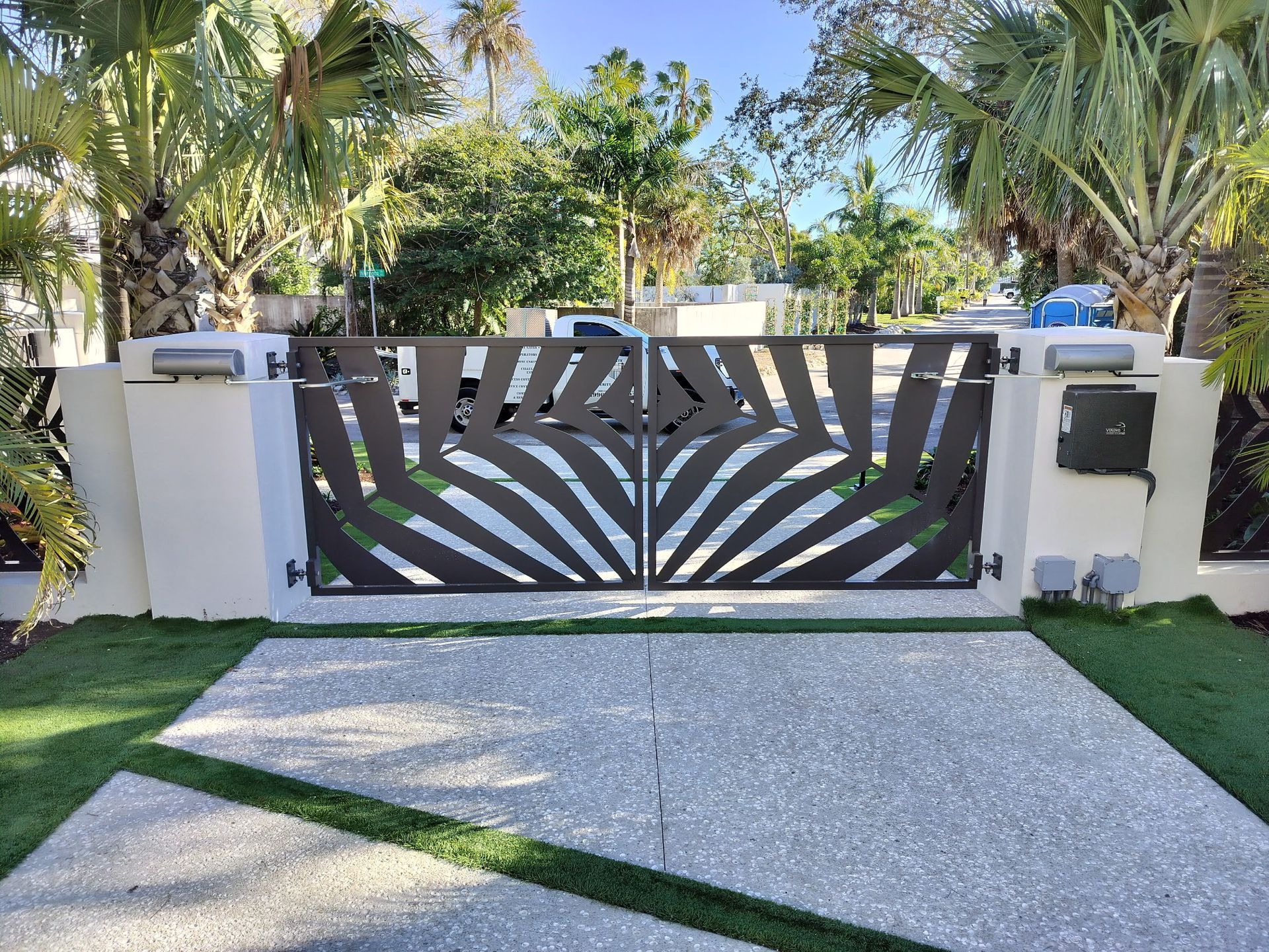 Decorative metal gate with a sunburst pattern at a driveway entrance.