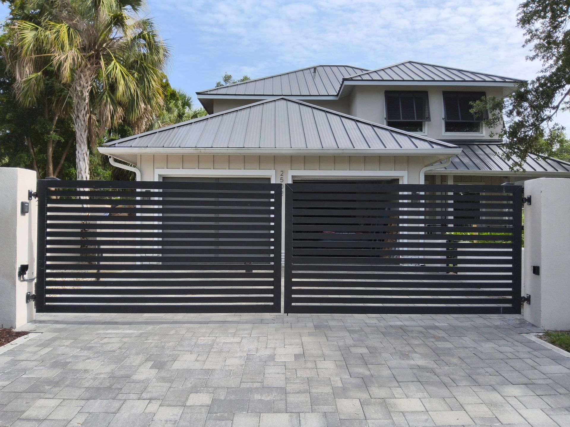 Black horizontal slat gates in front of a modern two-story house with a light gray paver driveway.
