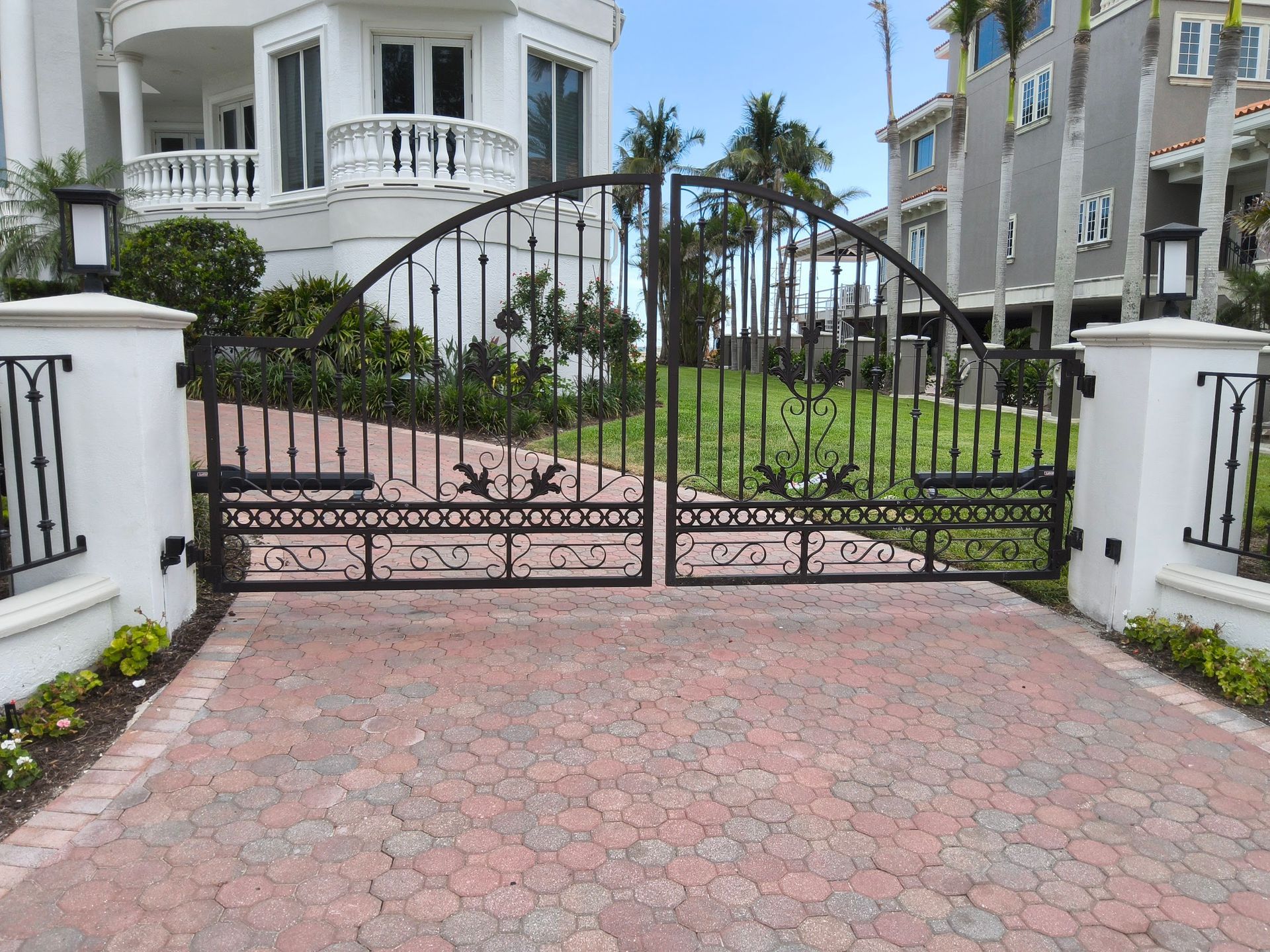 Black wrought iron driveway gates with brick paver drive and large white house.