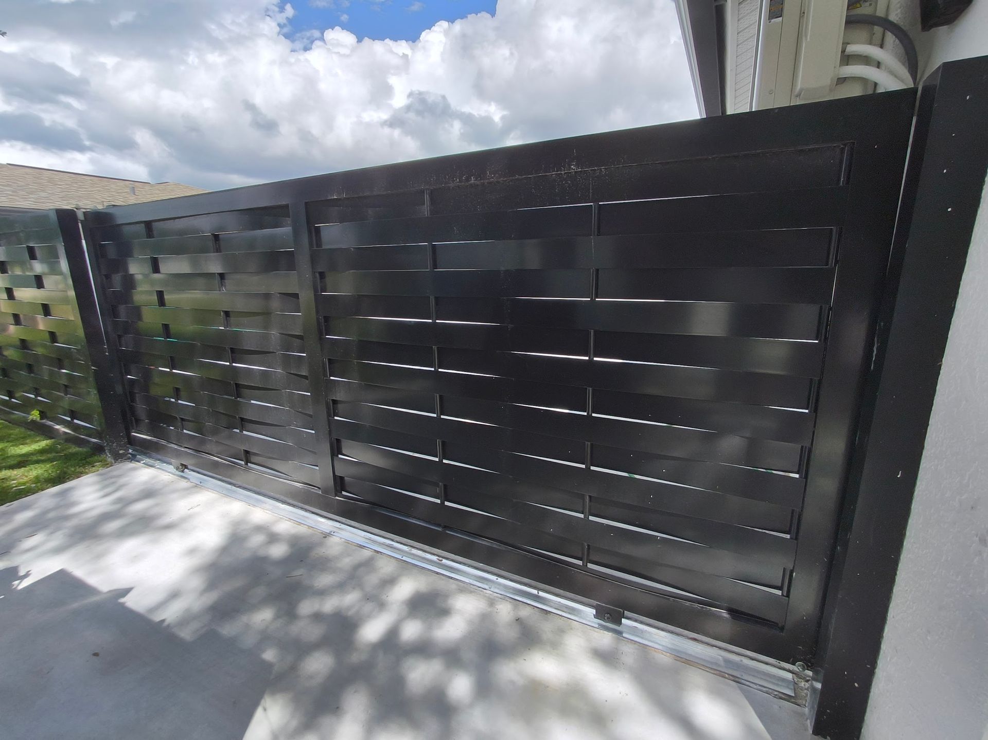 Black horizontal slat gate on a concrete surface, likely an entry to a property.