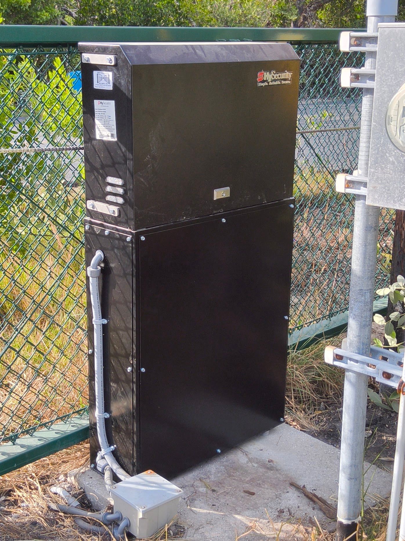Black rectangular electrical box, mounted outside, with a conduit and wiring.