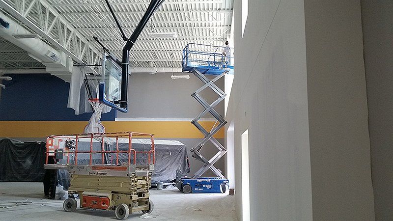 A basketball hoop is being installed in a gym with scissor lifts