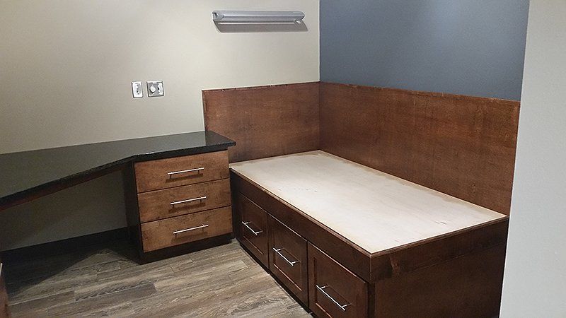 A room with a bed, desk, and drawers in it