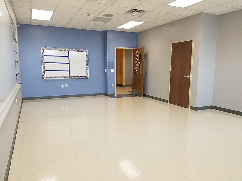 An empty classroom with a whiteboard on the wall and a door