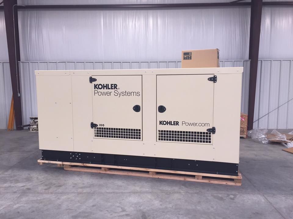 A beige industrial Kohler Power Systems generator sits on a wooden pallet inside a warehouse with metal walls.